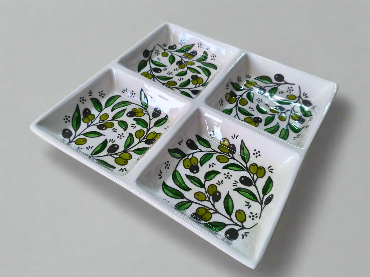 White ceramic tray with four compartments featuring green and black leaf patterns on a wooden surface.