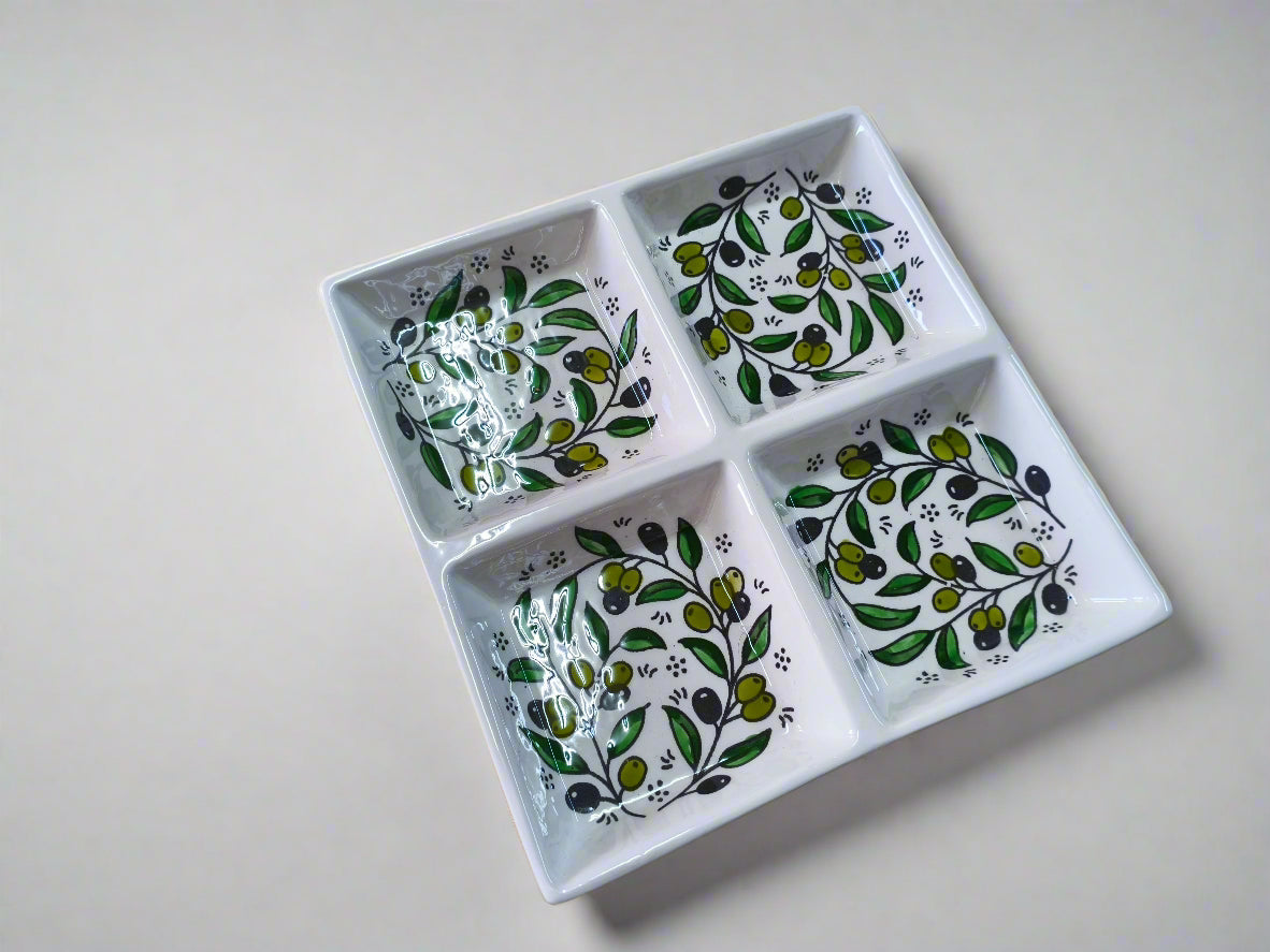 White ceramic dish with four compartments, each featuring green leaf patterns on a wooden surface.