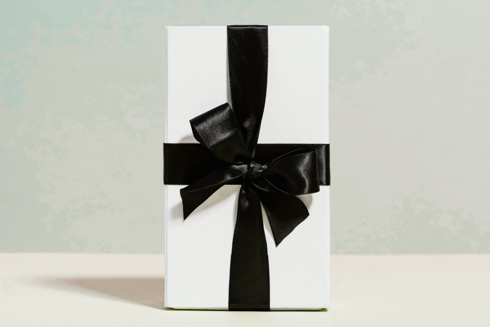 White gift box with a black ribbon on a light gray background
