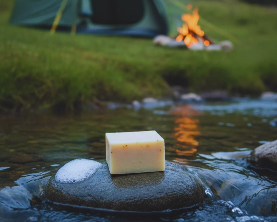 Bar of soap on a rock in a stream with a tent and campfire in the background