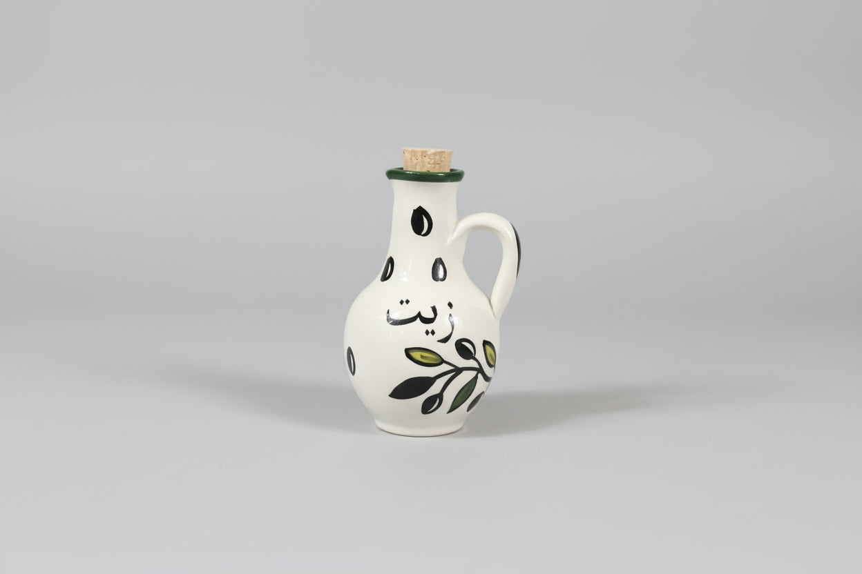 White ceramic oil bottle with black designs on a gray wooden floor