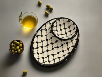 A handcrafted ceramic appetizer plate with a geometric pattern, displayed alongside a small bowl of olives and a glass of olive oil.